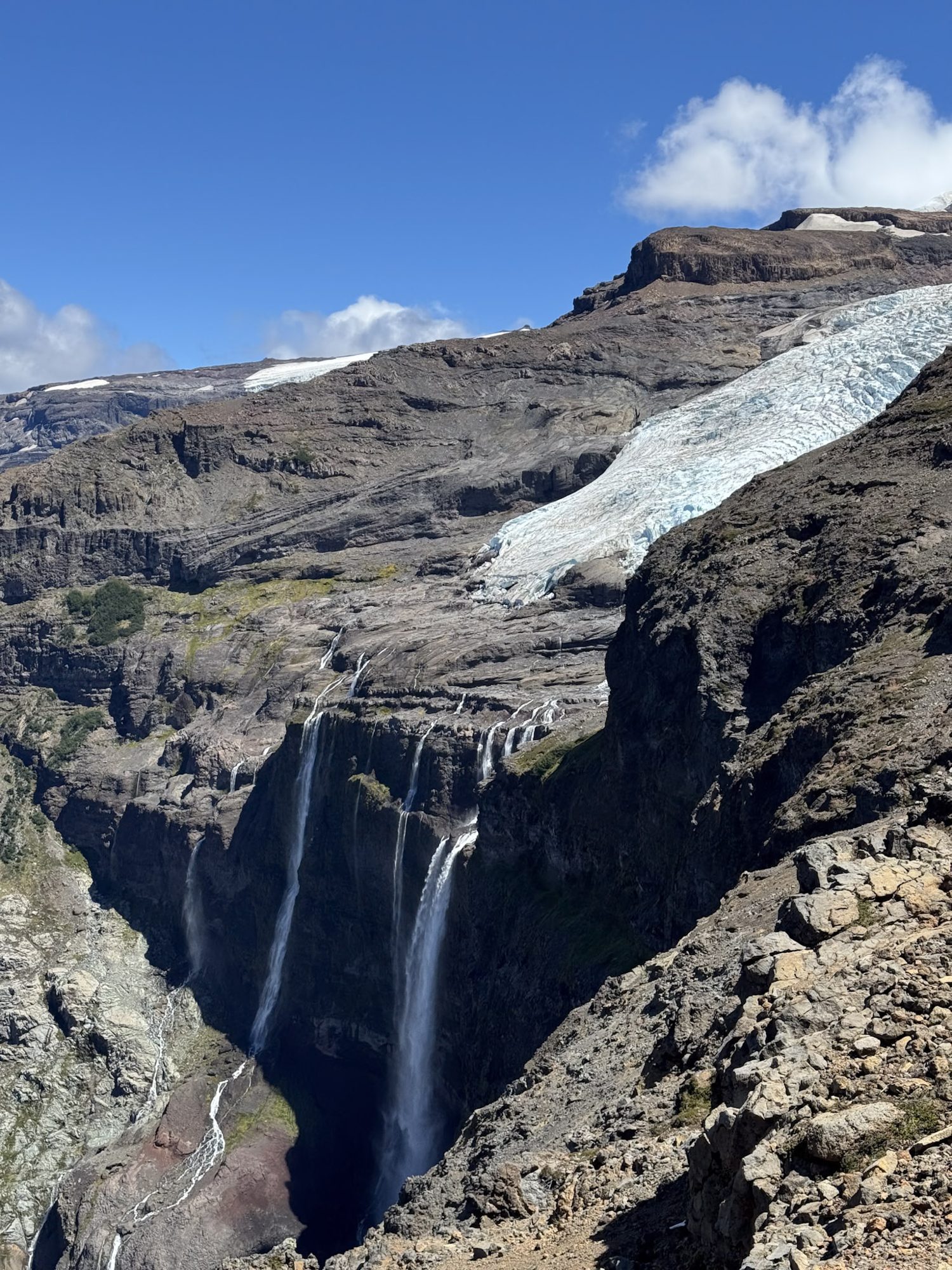 Cachoeira multi-quedas caindo de paredão rochoso com geleira azul ao fundo nas montanhas de Bariloche, Patagônia argentina