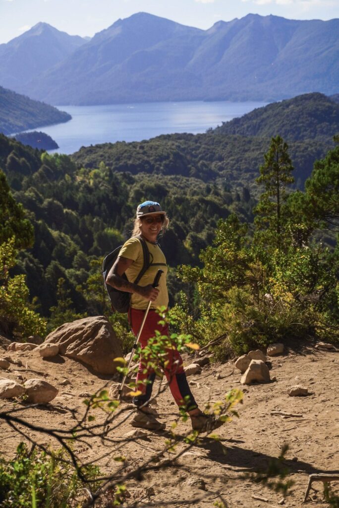 trilheiro caminhando em trilha de montanha com lago e floresta ao fundo em Bariloche