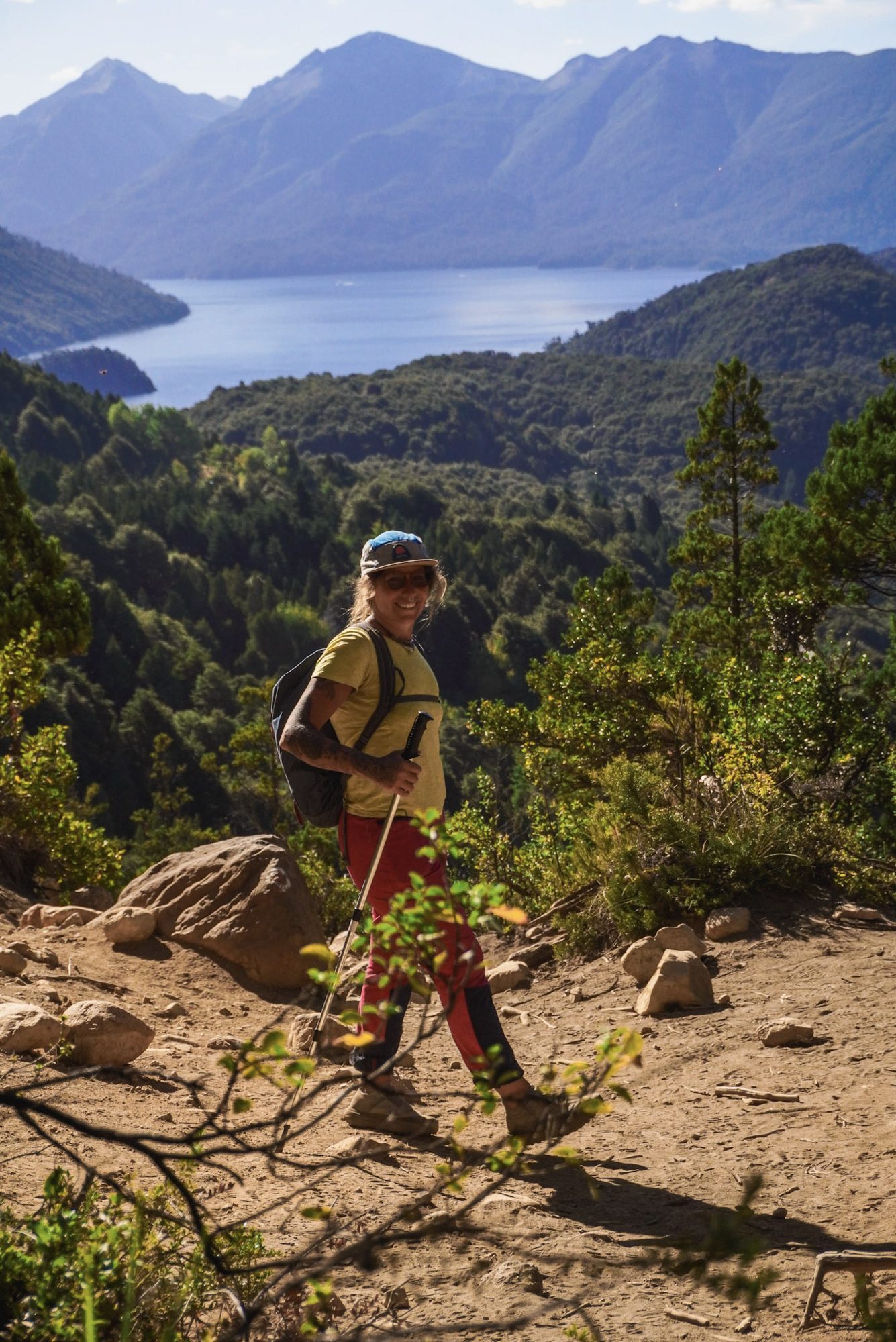trilheiro caminhando em trilha de montanha com lago e floresta ao fundo em Bariloche