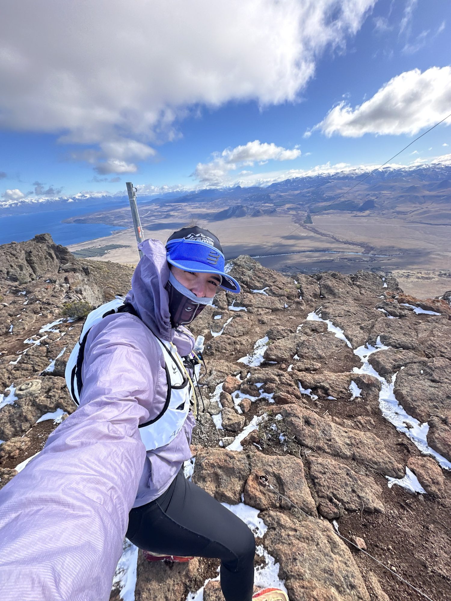 Mulher em selfie no topo de montanha rochosa com neve e lago ao fundo em Bariloche