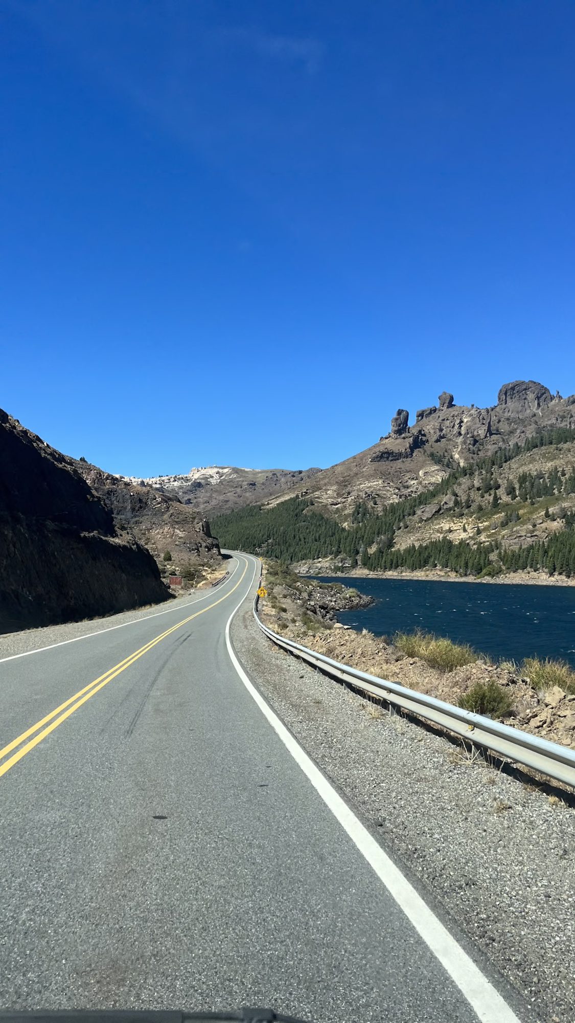Estrada à beira do lago com montanhas rochosas ao fundo em Bariloche