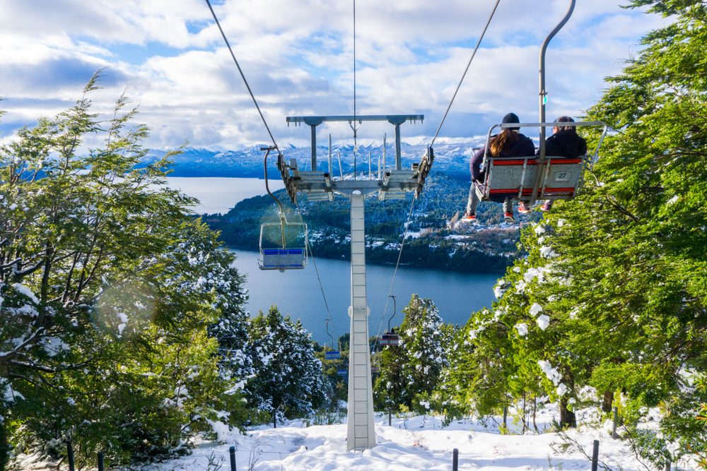 Bariloche em Julho: Mulher sorridente com óculos de sol coloridos em mirante com vista para vale nevado e montanhas em Bariloche - Vale Liberdade