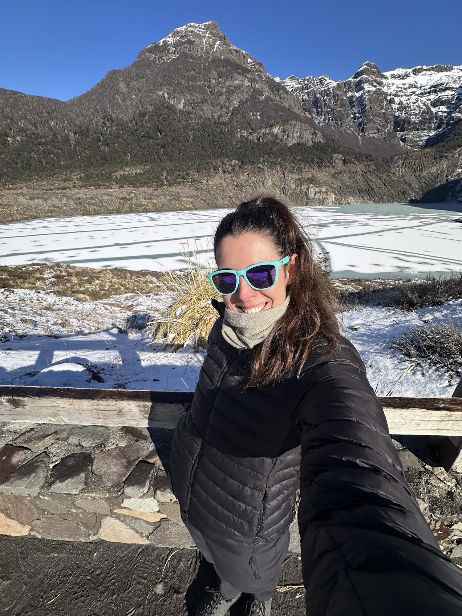 Bariloche em Julho: Mulher sorridente com óculos de sol coloridos em mirante com vista para vale nevado e montanhas em Bariloche - Vale Liberdade