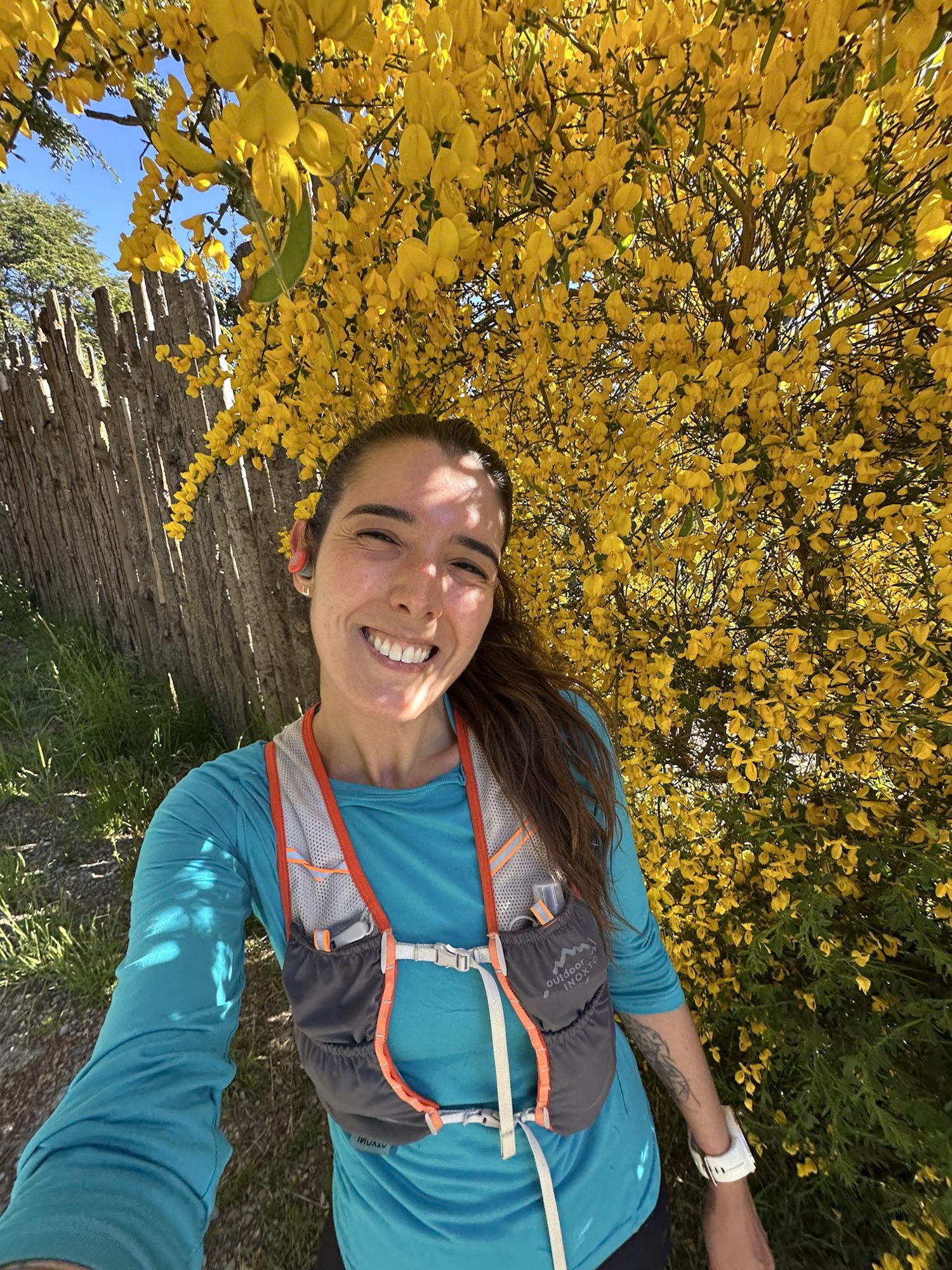 Bariloche na Primavera: Corredora sorri em selfie diante de arbusto com flores amarelas em Bariloche - Vale Liberdade