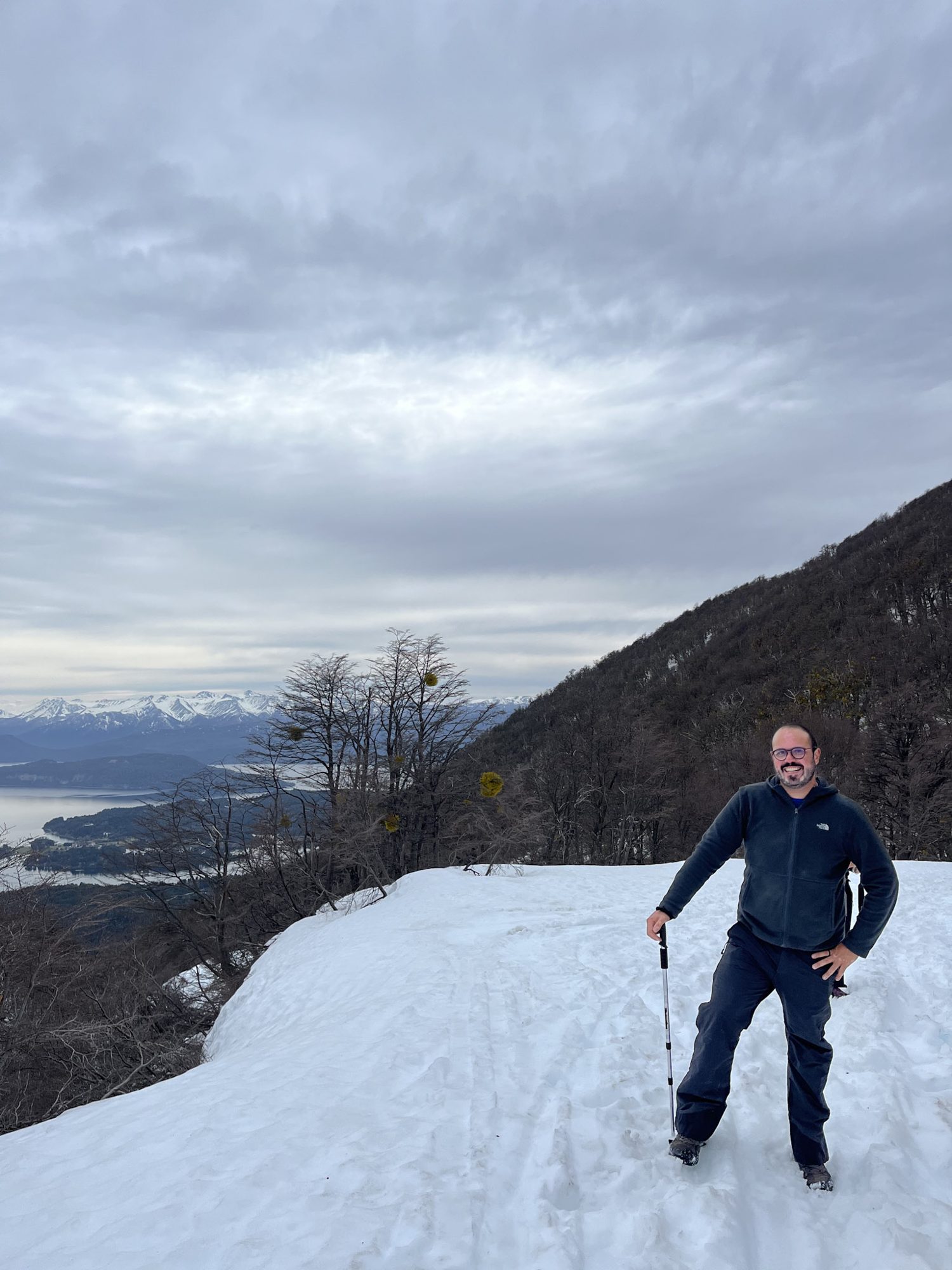 Homem posando em trilha coberta de neve com vista para lago e montanhas em Bariloche
