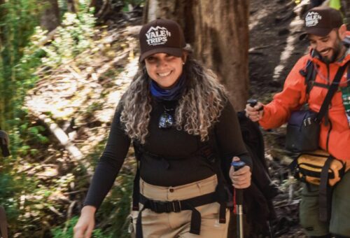 Trilheiros sorrindo com bastões em trilha de floresta patagônica durante trekking na região de Bariloche.