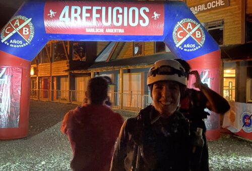 Corredora sorrindo sob a chuva na chegada da 4 Refugios Bariloche, à noite, com o arco inflável iluminado ao fundo.