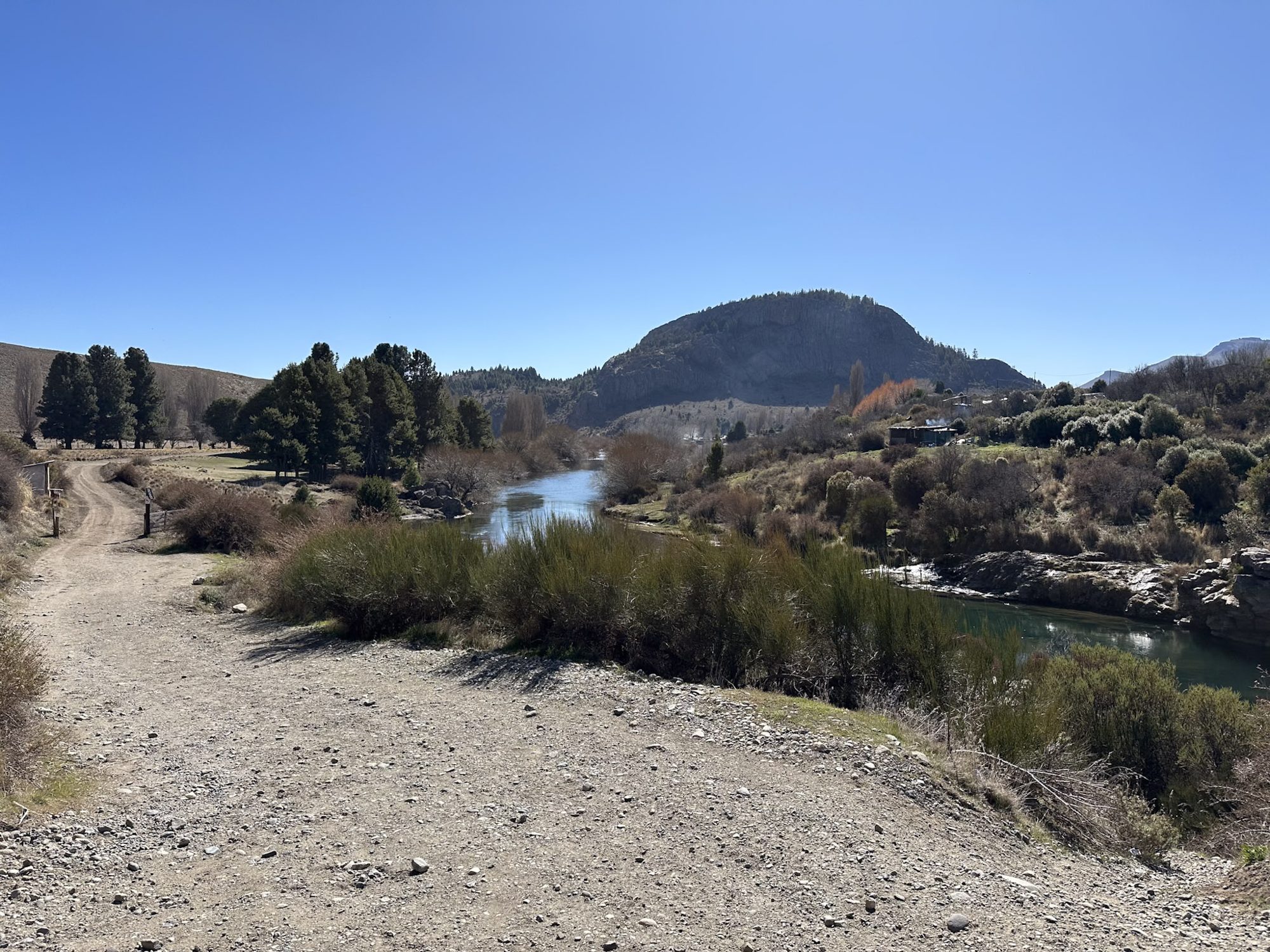 Mapuche: povo originário da Patagônia e sua contribuição à cultura de Bariloche - Bariloche para Brasileiros: Trilha de terra às margens de um rio com morro rochoso ao fundo em Bariloche - Vale Liberdade