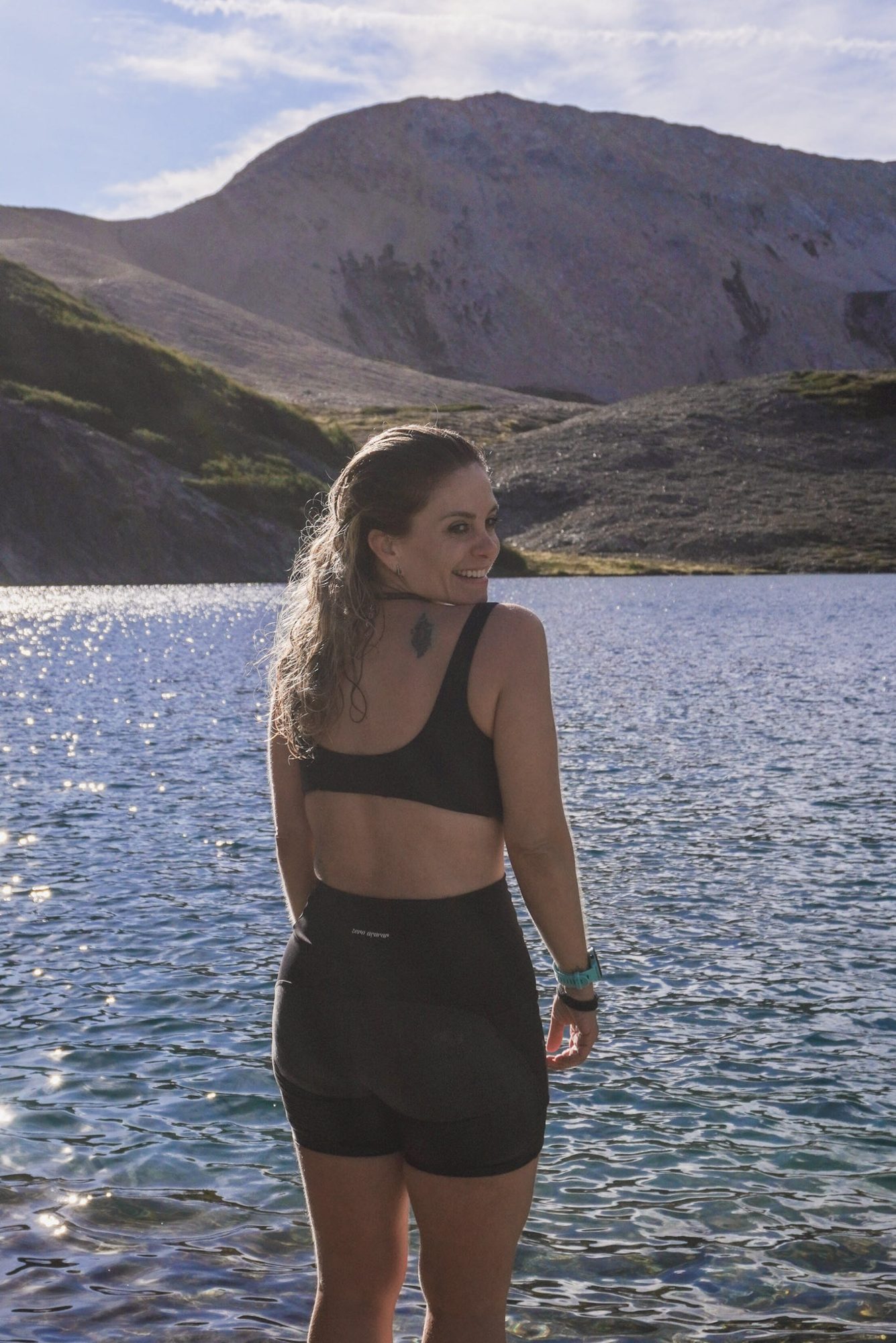 Correr em Bariloche: jovem de costas sorrindo à beira de lago com montanhas ao fundo em Bariloche - Vale Liberdade