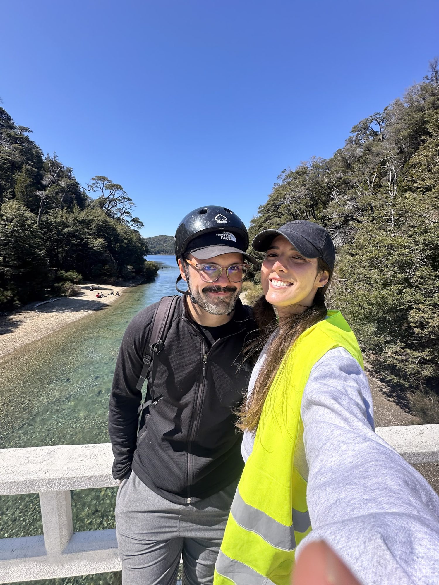Mapuche: povo originário da Patagônia e sua contribuição à cultura de Bariloche - Bariloche para Brasileiros: casal sorri para selfie em ponte com rio e floresta ao fundo em Bariloche - Vale Liberdade