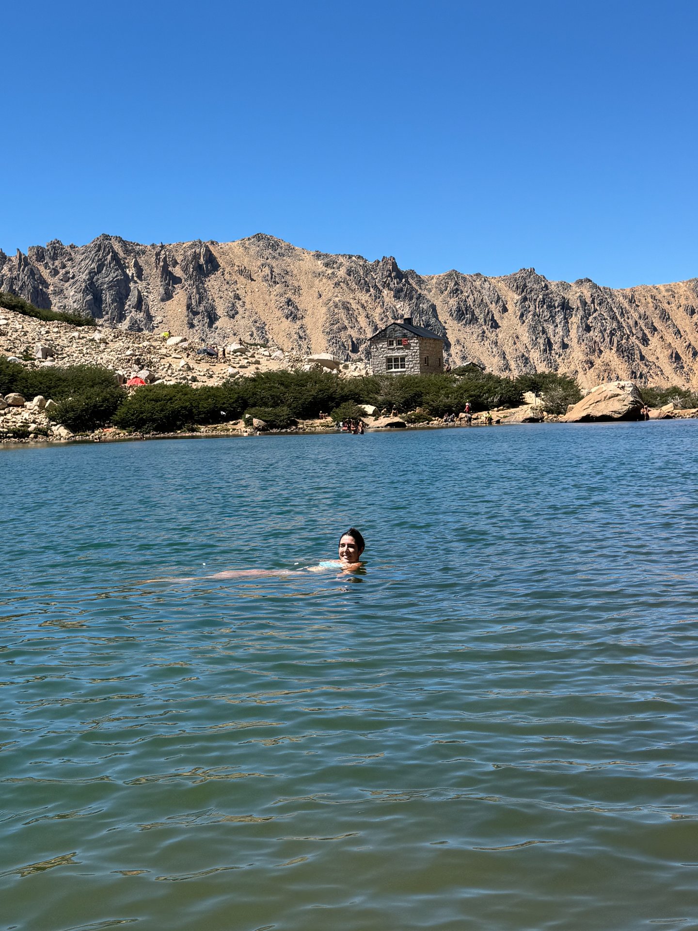 Pessoa nadando em lago alpino do Refúgio Frey no verão, representando os dias mais amenos e ativos em Bariloche.