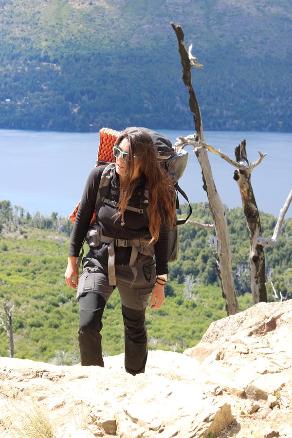 Mulher trekking com mochila vermelha passando por troncos na trilha