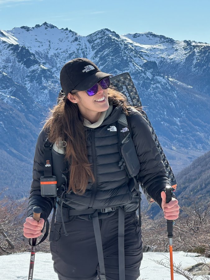 Mulher em trekking de inverno equipada com moletom, mochila, bastões e óculos