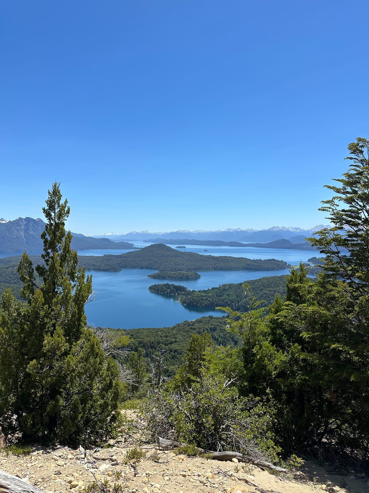 Vista do Lago Nahuel Huapi a partir de um mirante de Bariloche, com ilhas, mata nativa e céu azul de verão.