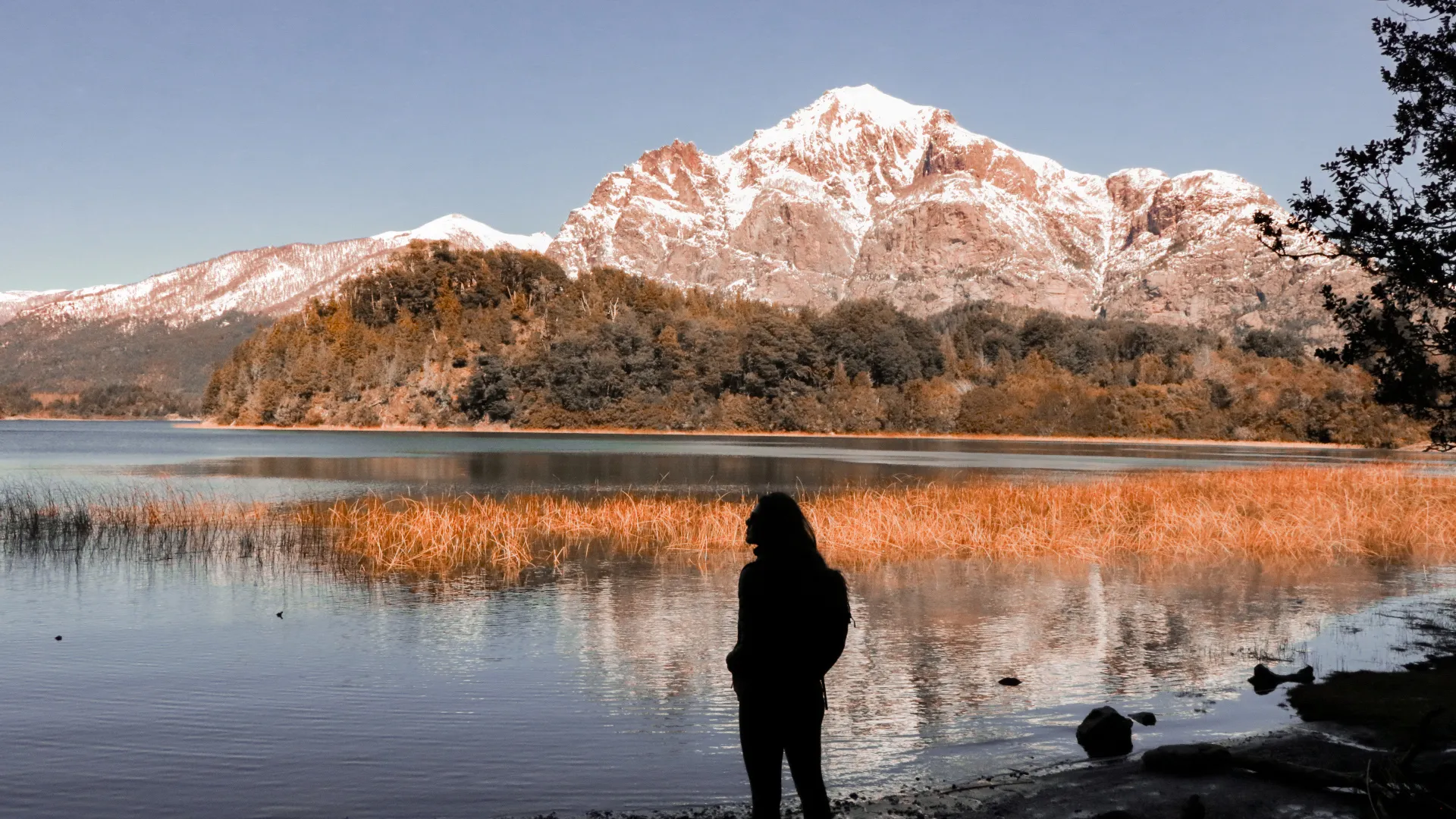 bariloche em abril: Pessoa contemplando lago patagônico com montanha coberta de neve e vegetação de outono em Bariloche, Argentina