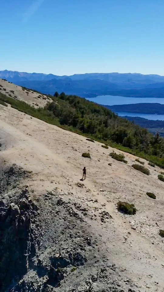 bariloche em março: Pessoa caminhando em encosta rochosa com vista para o Lago Nahuel Huapi e as montanhas dos Andes em Bariloche, Patagônia argentina