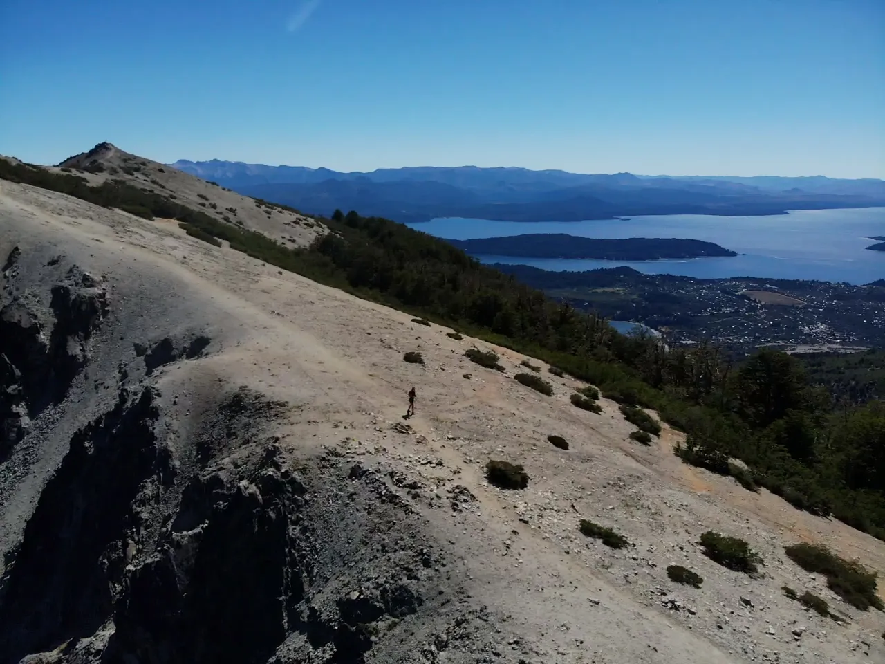 bariloche em março: Trilheiro subindo a encosta de pedra do Cerro Otto com vista do Lago Nahuel Huapi e Bariloche em dia de céu limpo na Patagônia argentina