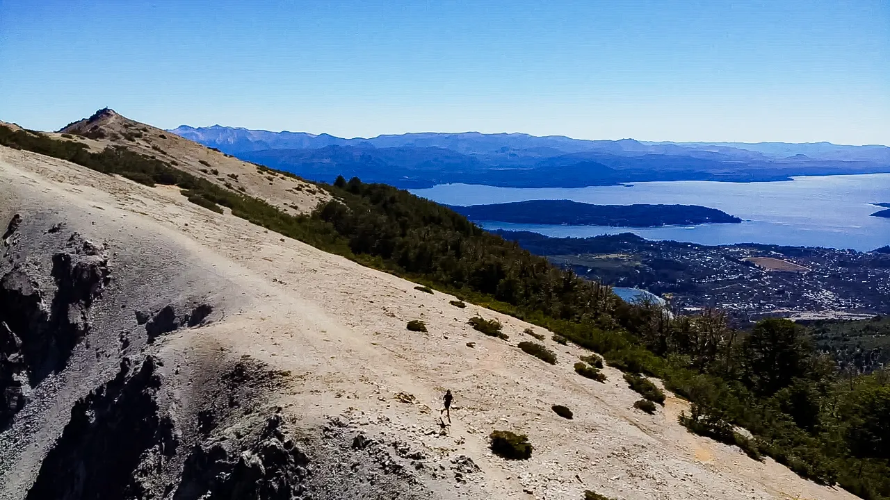 bariloche em março: Vista panorâmica de Bariloche e o Lago Nahuel Huapi fotografada do alto da encosta pedregosa do Cerro Otto, com trilheiro ao centro