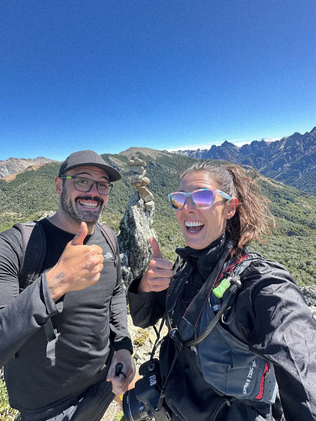 cerro campanario: Casal sorridente com joinha no topo de trilha em Bariloche, com montanhas da Patagônia argentina ao fundo