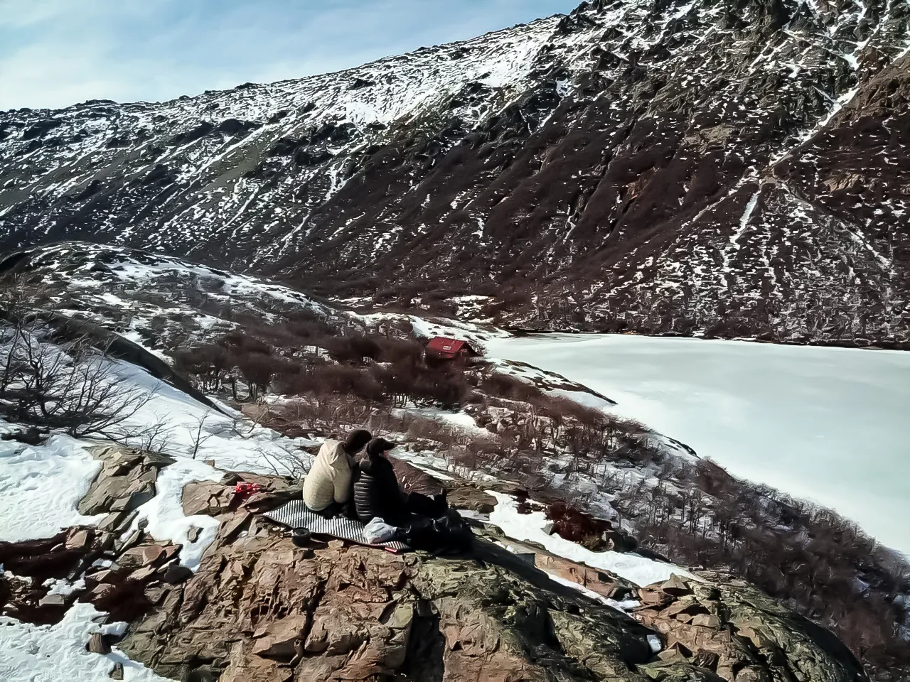 o que é trekking: Casal admirando lago congelado cercado por montanhas nevadas durante trekking de inverno em Bariloche, Patagônia argentina