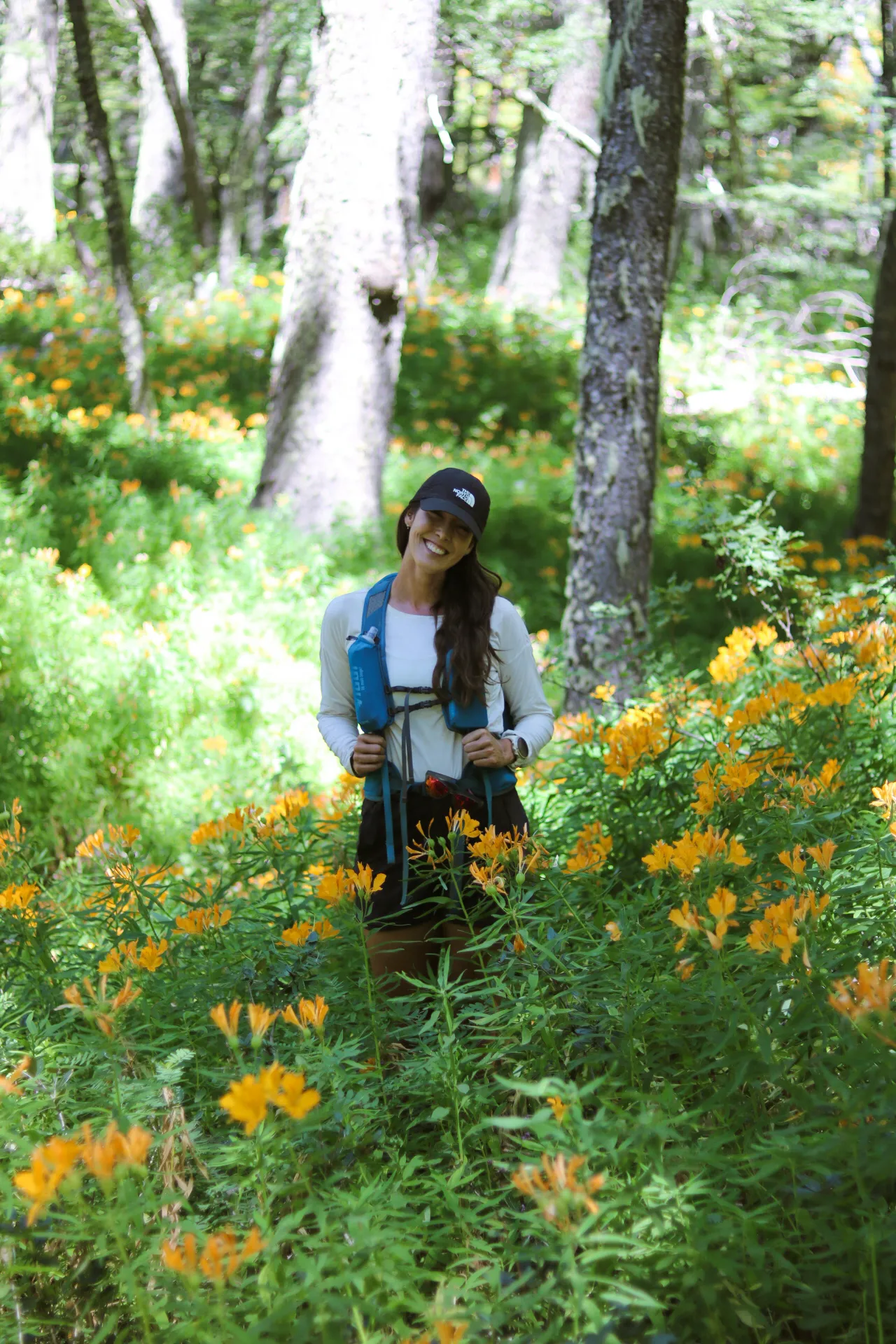 patagonia run: Mulher fazendo trilha em floresta de Bariloche cercada de flores silvestres laranja no verão patagônico