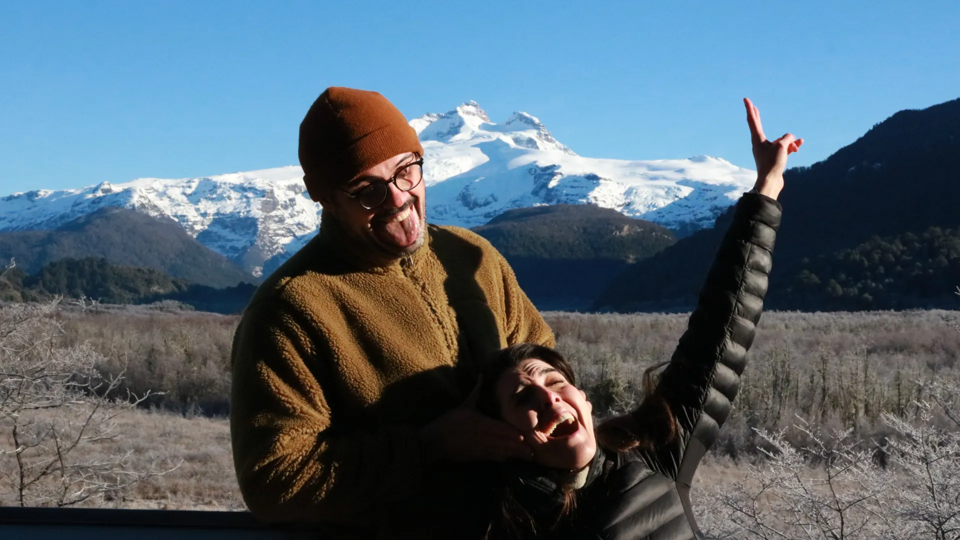 patagonia run: Casal sorrindo e brincando com montanha nevada e céu azul ao fundo em Bariloche, Patagônia argentina