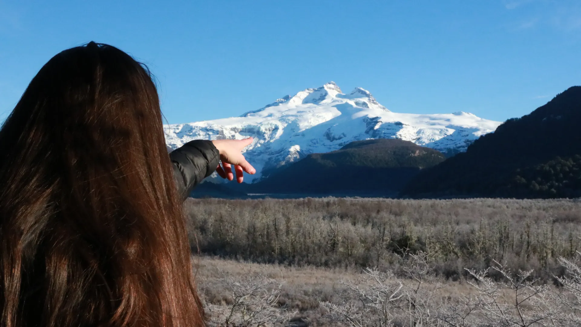 Precisa de Visto para Bariloche? Regras para Brasileiros: Mulher aponta para o vulcão Tronador com cume nevado ao fundo, no Parque Nacional Nahuel Huapi, Bariloche