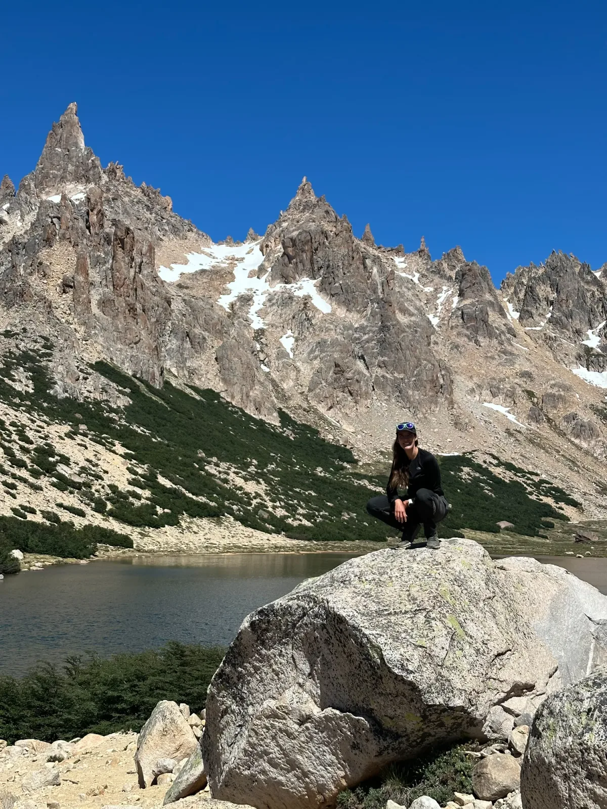 quanto custa viagem bariloche: Trilheiro descansando em rocha no Lago Toncek com as torres do Cerro Catedral e neve ao fundo, Bariloche, Patagônia argentina