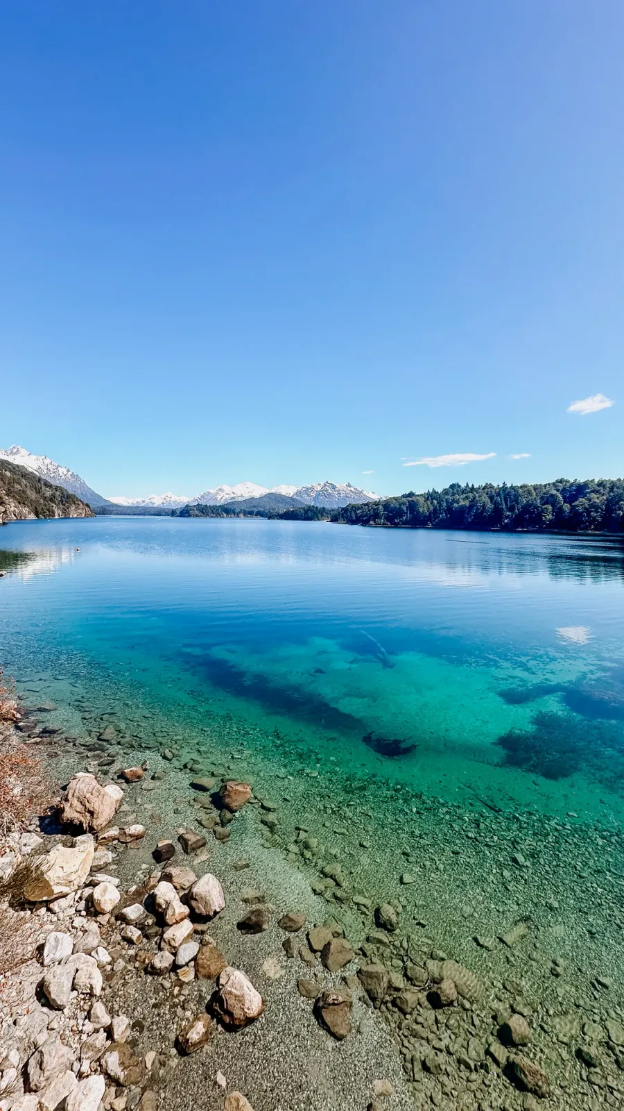 roteiro bariloche inverno: Lago de águas cristalinas turquesa em Bariloche, Patagônia argentina, com montanhas nevadas e floresta ao fundo